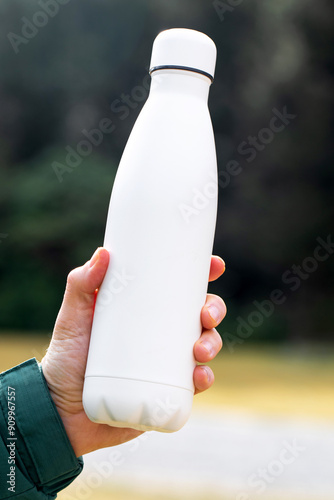 man holds mockup thermos against blurry bushes closeup photo