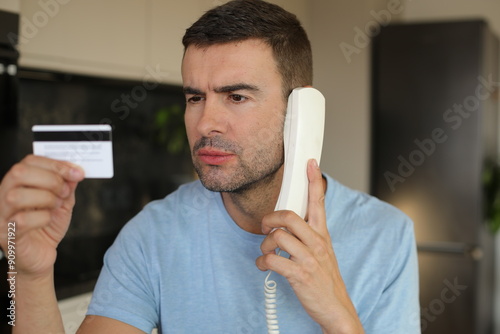 Skeptical looking man holding credit card during phone call 