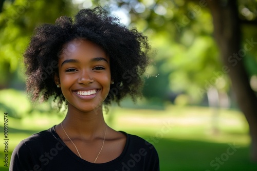 Smiling young woman with natural curly hair in sunny park, showcasing happiness, outdoor joy concept