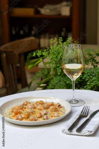 Fine dining table setup with a plate of risotto and a glass of white wine. Concept of upscale restaurant, gourmet meal, and elegant culinary experience. High quality photo