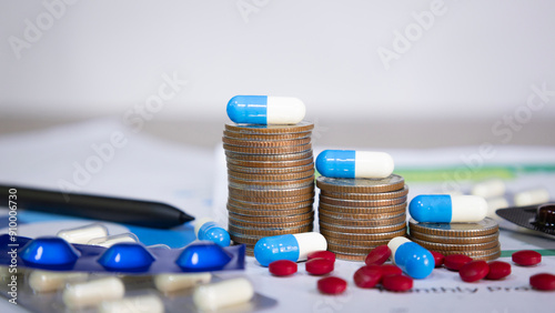 Blue and white capsules on and around a stack of coins, meaning health insurance, medical expenses and medicine, finance, saving money, business, financial and medical healthcare concepts.