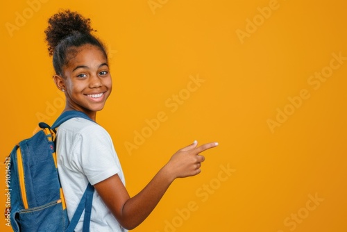 Smiling African American girl with curly hair, pointing to the side, wearing a blue backpack and white shirt against a yellow background.