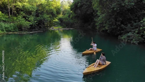 Young couple is enjoying a relaxing ride on wooden surfboards on the river. Aerial footage photo