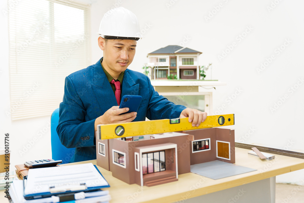 Asian architect in a formal suit works alone at his desk with a laptop, paperwork, tablet, and calculator, drawing blueprints for a home and land mortgage project. Asian architect in a formal suit works alone at his desk with a laptop, paperwork, tablet, and calculator, drawing blueprints for a home and land mortgage project.