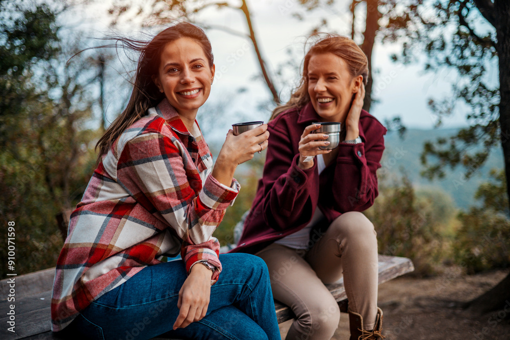Female friends sitting under a tree in the forest and eating lunch. Women are holding water bottles and chatting on a hike, enjoying a break Female friends sitting under a tree in the forest and eating lunch. Women are holding water bottles and chatting on a hike, enjoying a break