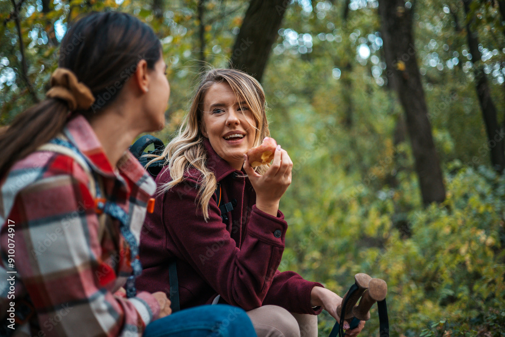 Female friends sitting under a tree in the forest and eating lunch. Women are holding water bottles and chatting on a hike, enjoying a break, surrounded by lush greenery and fallen trees. Female friends sitting under a tree in the forest and eating lunch. Women are holding water bottles and chatting on a hike, enjoying a break, surrounded by lush greenery and fallen trees.