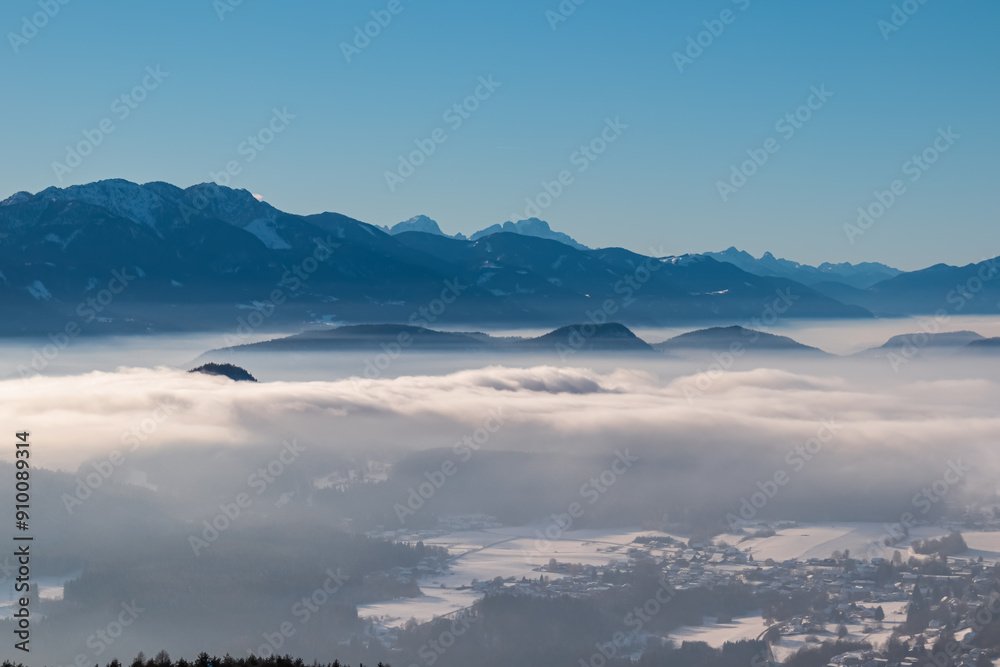 Panoramic view of snowcapped mountain peak Mangart in winter seen from tower Pyramidenkogel, Carinthia, Austria. Fog covered alpine valley surrounded by majestic Austrian Alps. Mystical atmosphere Panoramic view of snowcapped mountain peak Mangart in winter seen from tower Pyramidenkogel, Carinthia, Austria. Fog covered alpine valley surrounded by majestic Austrian Alps. Mystical atmosphere