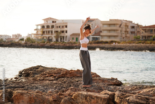 Relaxed woman enjoying summer sunny day in Mallorca island, dancing on the rocks near the sea. Freedom concept. photo