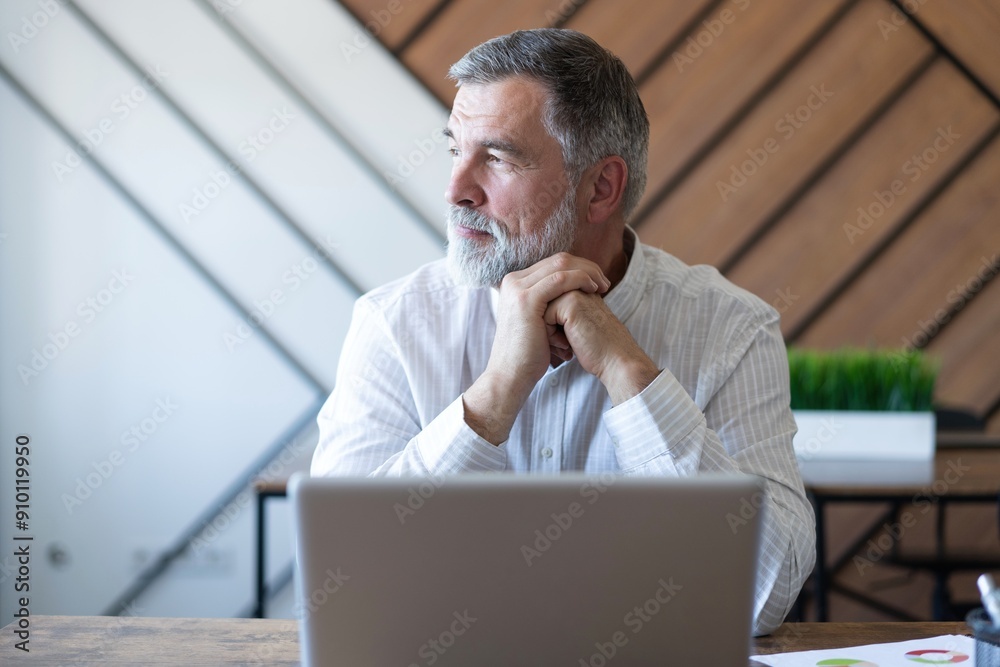 Smiling mature business man executive wearing shirt sitting at desk using laptop. Happy busy professional middle aged manager investor working on computer looking away in office Smiling mature business man executive wearing shirt sitting at desk using laptop. Happy busy professional middle aged manager investor working on computer looking away in office