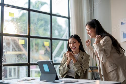 Two businesswoman celebrating success while looking at laptop in modern office