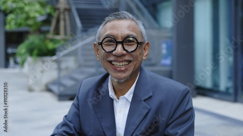 Portrait of the Senior Handsome Businessman in Glasses Wearing Formal Suit. Successful Teacher Looking at the Camera while Sitting on the Business Centre. Business and People Concept photo