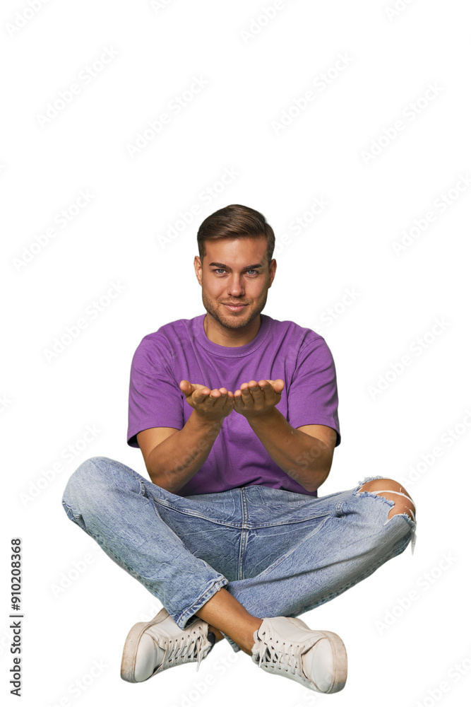 Casual man sitting on floor holding something with palms, offering to camera. Casual man sitting on floor holding something with palms, offering to camera.