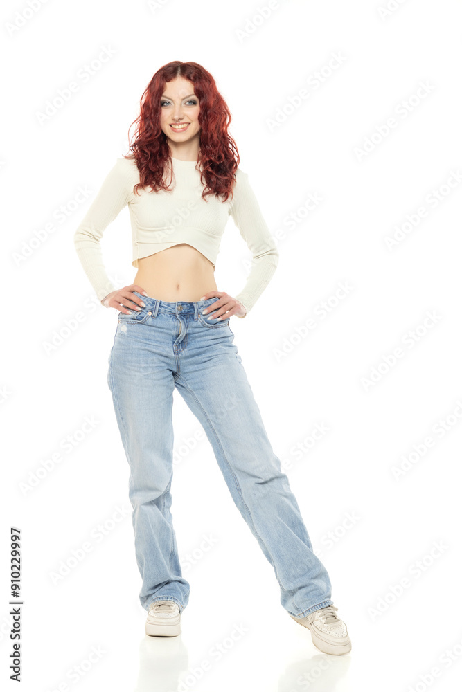 Charming young redhead woman posing in studio in white short blouse and blue jeans. Charming young redhead woman posing in studio in white short blouse and blue jeans.