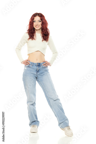 Charming young redhead woman posing in studio in white short blouse and blue jeans.