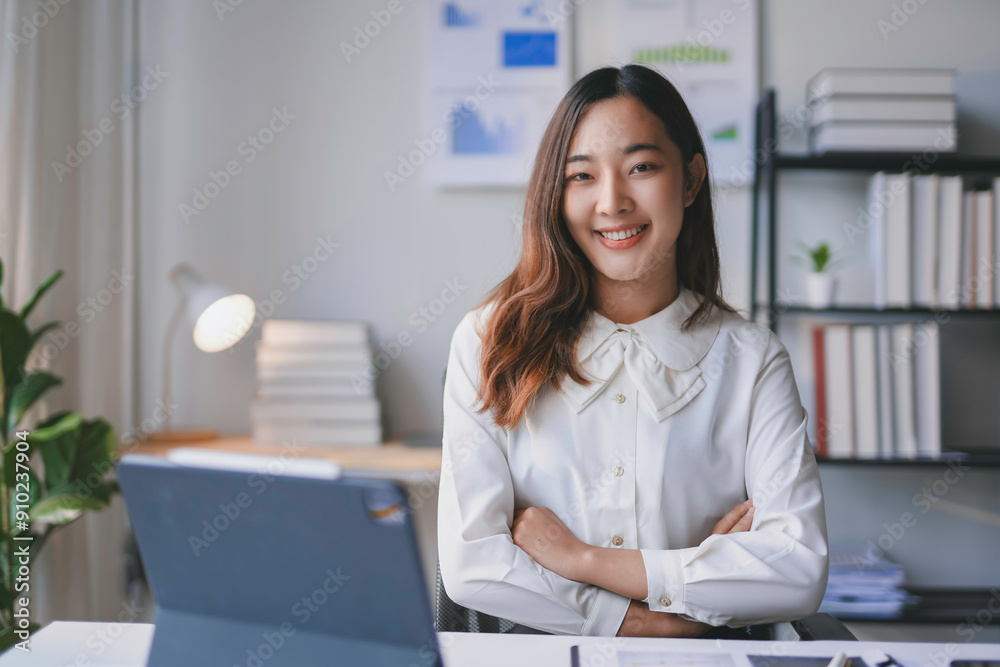Young asian businesswoman smiling while sitting at her desk with her arms crossed in a modern office