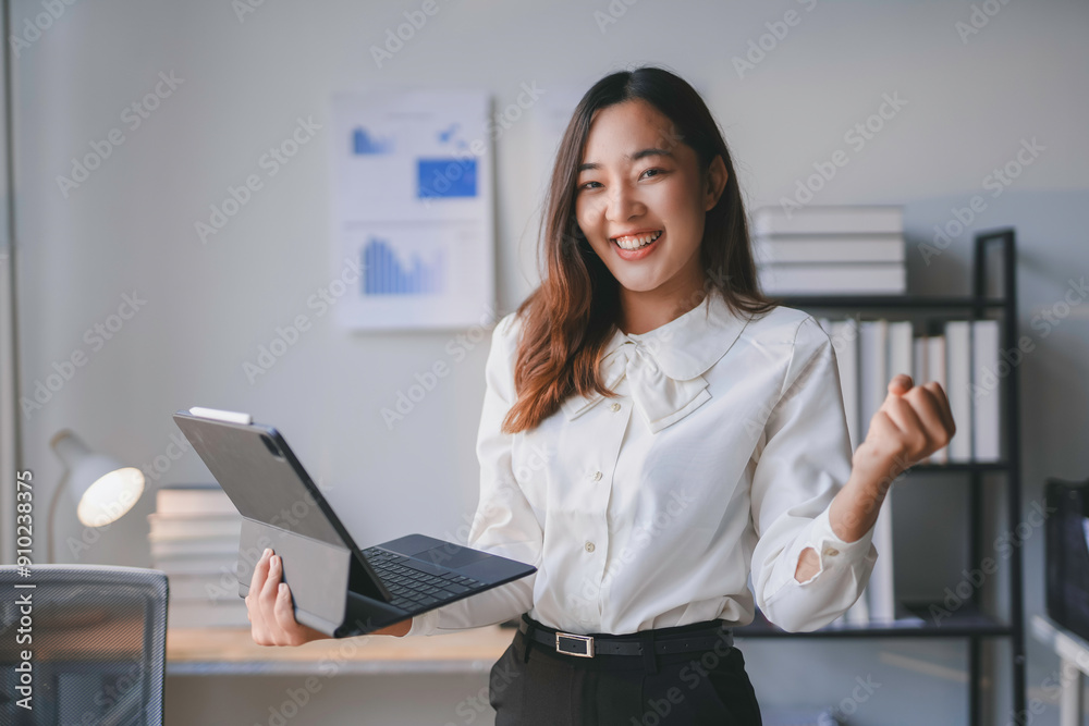 Excited businesswoman holding a tablet and raising her fist in a modern office celebrating success Excited businesswoman holding a tablet and raising her fist in a modern office celebrating success