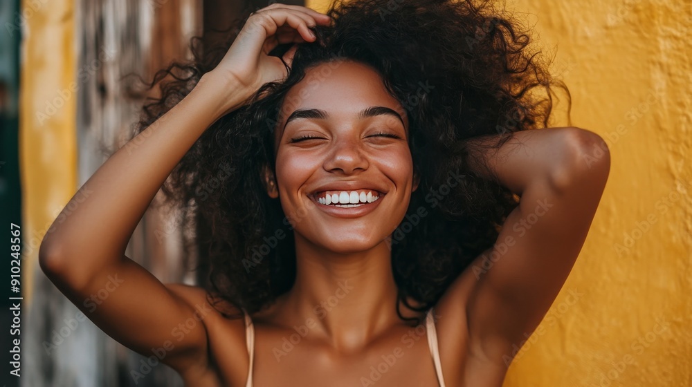 Joyful young woman of mixed ethnicity with curly hair smiles brightly against a vibrant yellow backdrop.