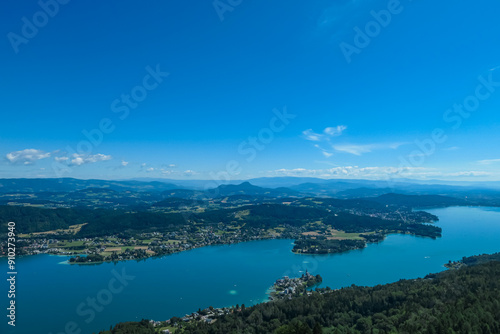 Aerial panoramic view of Lake Wörthersee seen from Pyramindenkogel in Carinthia, Austria. Serene turquoise waters, lush green forests and rolling hills of Austrian Alps. Charming lakeside village