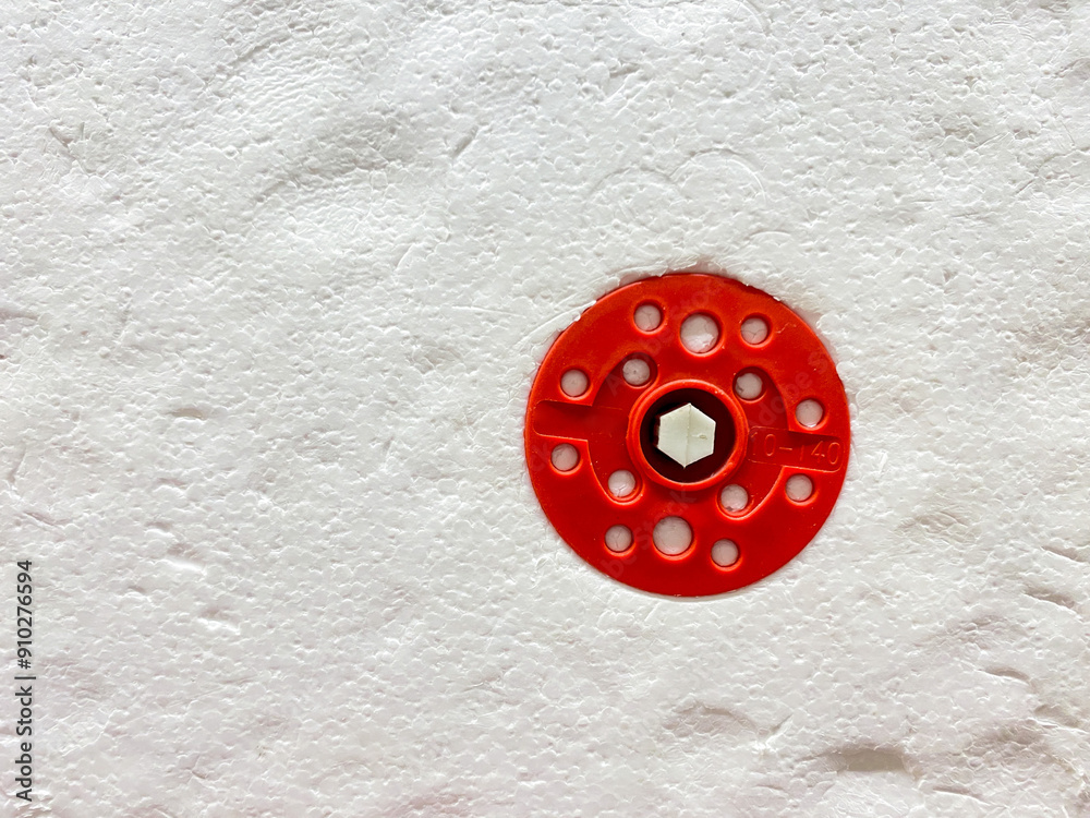 On a pristine white wall, there is a striking red circle that has multiple holes punctuated within its design, creating a visually interesting contrast with the background surface