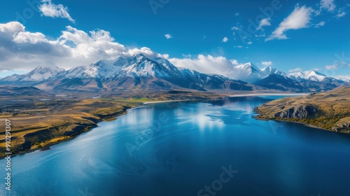 Aerial view of snow-capped mountains reflecting in a clear blue lake under a bright sky, capturing the serene natural beauty..