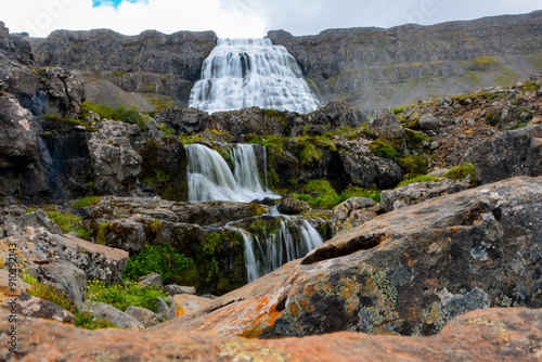 Cascades of Dynjandi Foss, a beautiful huge waterfall in the westfjords of Iceland with red rock in the foreground