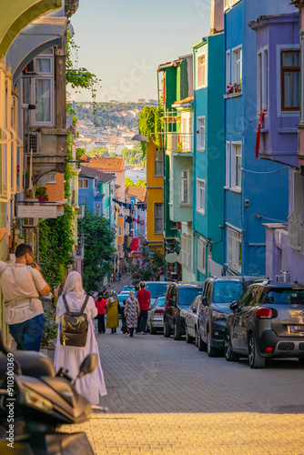 Photography Colorful urban street with people walking, parked cars, vibrant buildings, livel