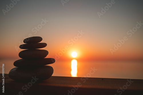 Tablou pe pânză A cairn of stones against the background of a sunset or an entrance to the sea