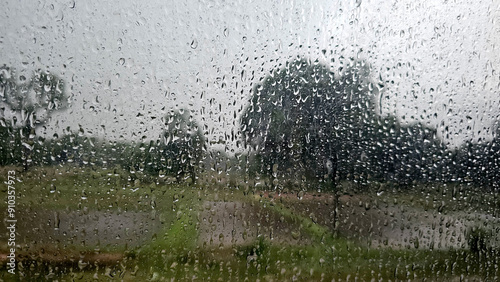 Raindrops on a window with a blurred view of flooded fields and trees, capturing the essence of a heavy rainstorm