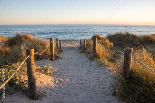 Sandy path leading to Son Bou beach, with the golden hues of the sun setting over the sea. Menorca, Spain