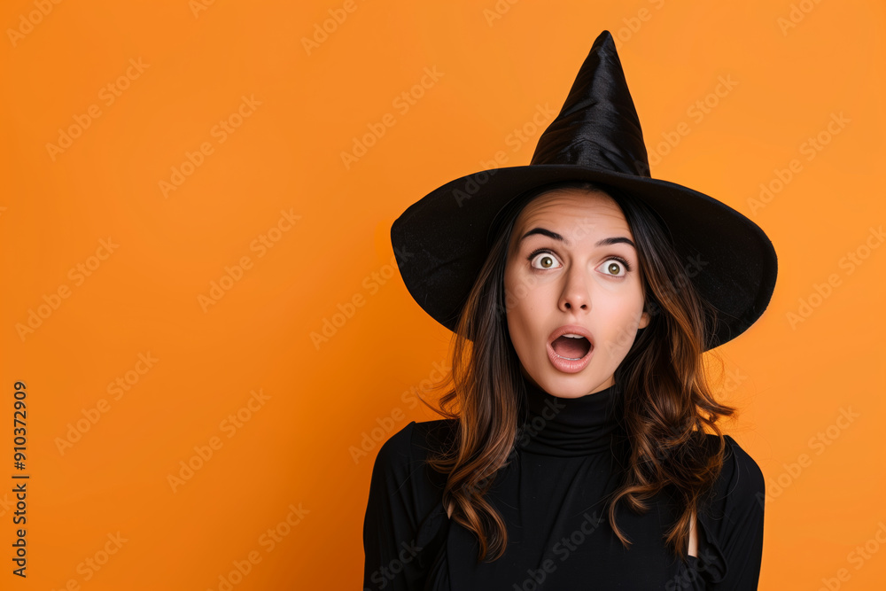 Woman dressed in black, wearing a witch's hat and looking surprised against an orange background. copy space Woman dressed in black, wearing a witch's hat and looking surprised against an orange background. copy space