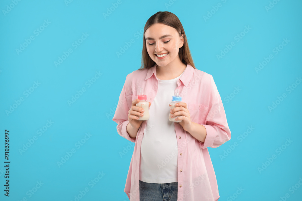 Expecting twins. Pregnant woman holding two bottles with milk on light blue background Expecting twins. Pregnant woman holding two bottles with milk on light blue background