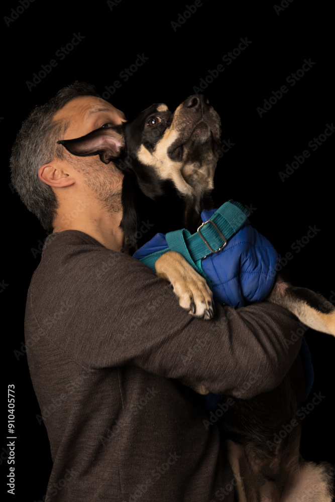 Obraz premium A man is hugging a dog wearing a blue jacket