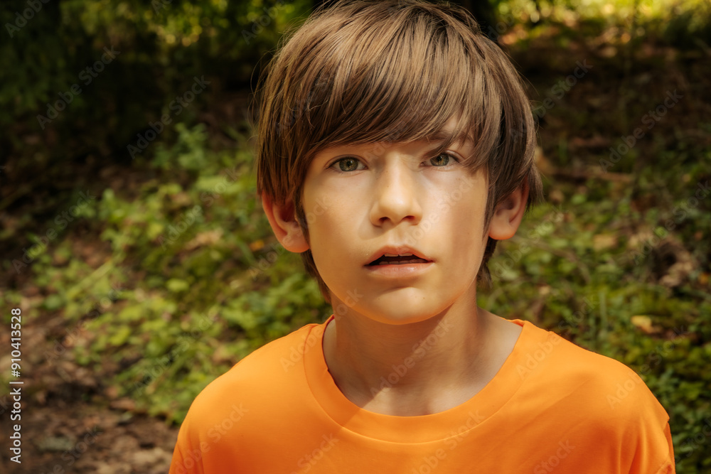 A young boy with brown hair and an orange shirt gazes intently in a forest setting. The background features lush greenery, capturing a moment of wonder and curiosity. A young boy with brown hair and an orange shirt gazes intently in a forest setting. The background features lush greenery, capturing a moment of wonder and curiosity.