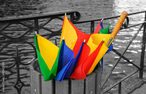 Broken colorful umbrella in garbage can after sudden storm at Annecy lake, France. Climate change concept. Overcast,  rainy weather, flood danger background. Retro black white selective color photo.