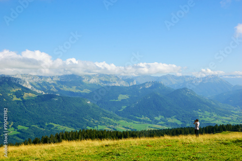 Young man taking picture of stunning summer landscape in French Alps mountains. Annecy lake area, Haute-Savoie, France.  Nature travel background banner.