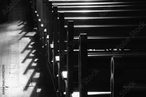 Rows of church benches. Sunlight filtered through the stained glass window. Selective focus. Religious background. Divine light, grace, hope, miracle concepts. Black white historic photo.