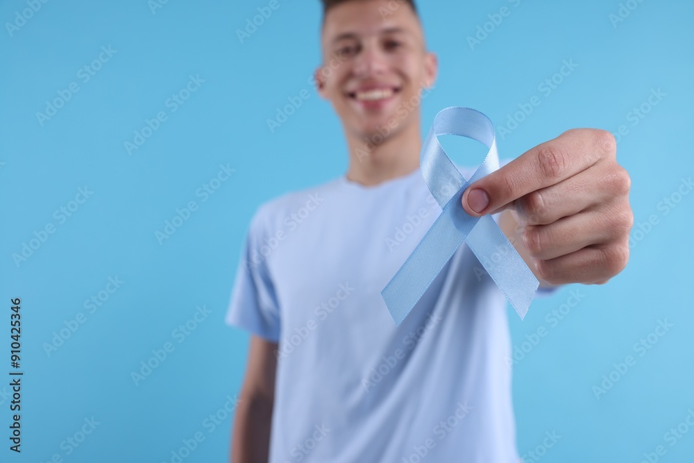 Prostate cancer awareness. Man holding light blue ribbon as symbol of support on color background, selective focus Prostate cancer awareness. Man holding light blue ribbon as symbol of support on color background, selective focus