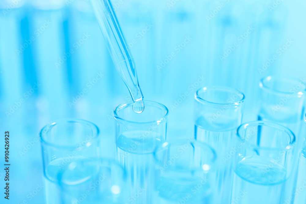 Dripping liquid from pipette into test tube on light blue background, closeup Dripping liquid from pipette into test tube on light blue background, closeup