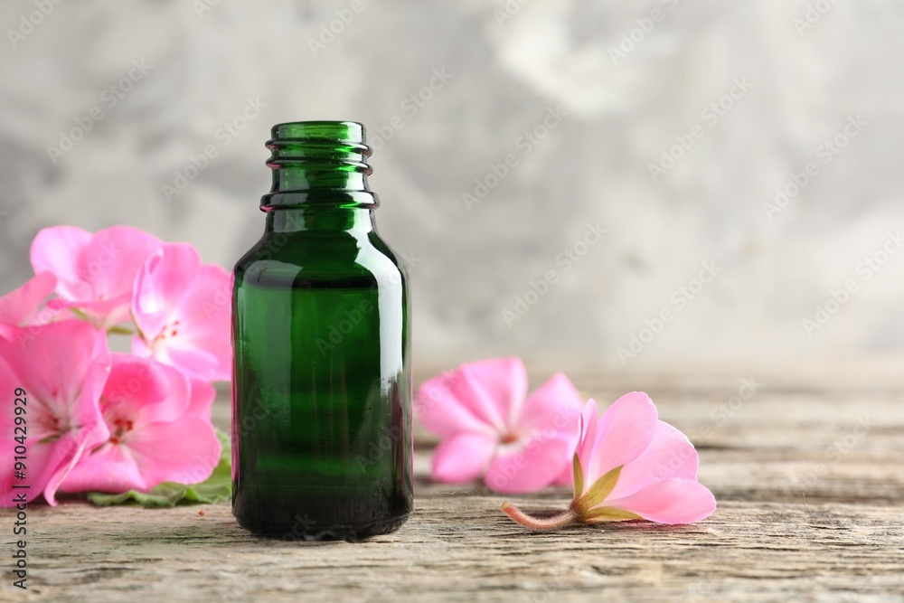 Bottle of geranium essential oil and beautiful flowers on wooden table, closeup. Space for text Bottle of geranium essential oil and beautiful flowers on wooden table, closeup. Space for text