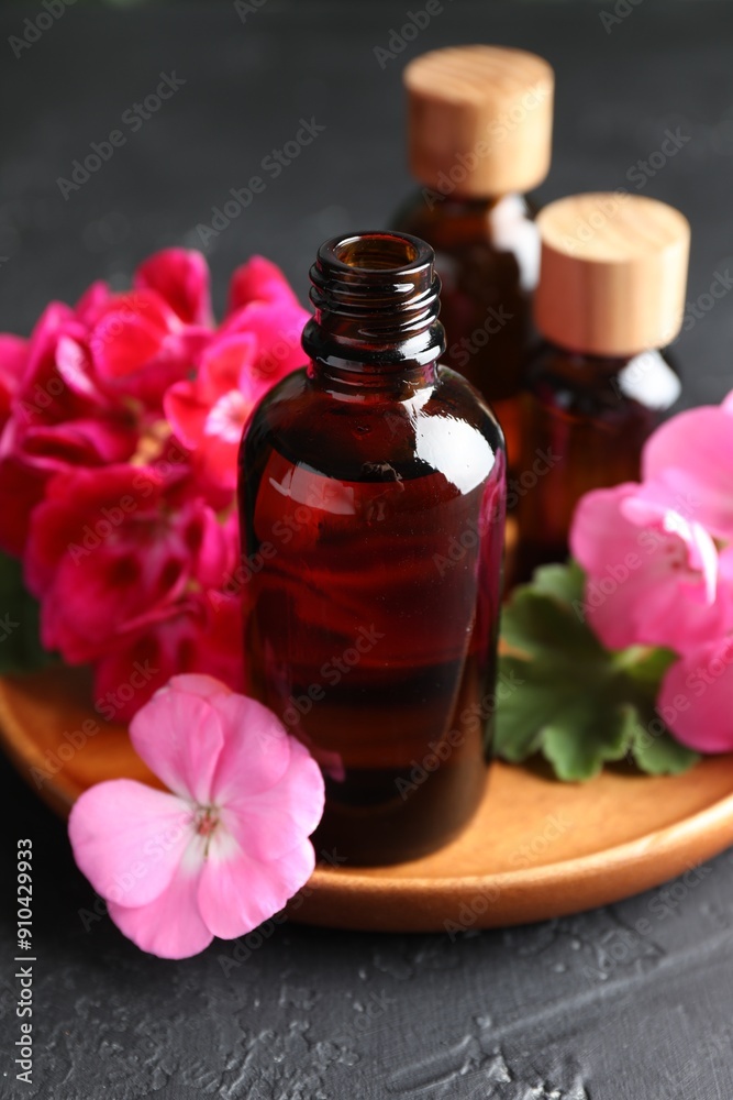 Bottles of geranium essential oil and beautiful flowers on black table, closeup Bottles of geranium essential oil and beautiful flowers on black table, closeup