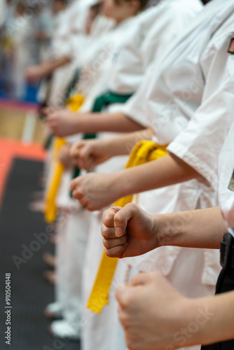 A close-up of a row of children in white karate kimonos with clenched fists.