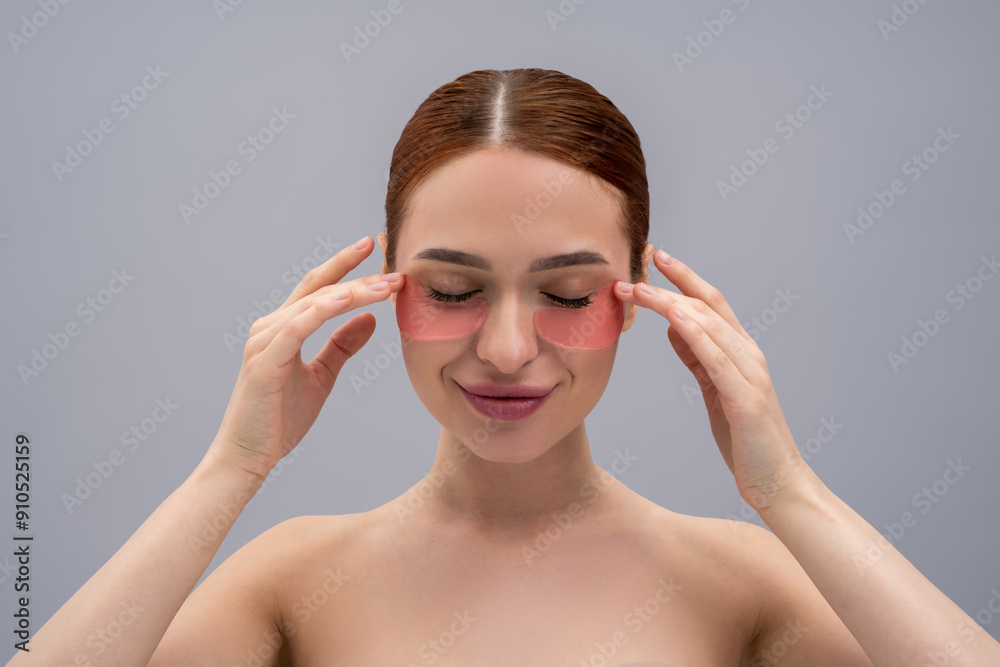 Cute young woman using beauty patches under her eyes and looking contented Cute young woman using beauty patches under her eyes and looking contented