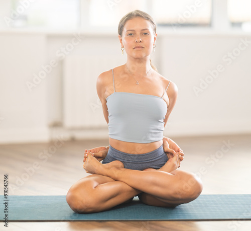 Young woman practicing agni stambhasana yoga pose on mat in fitness studio photo