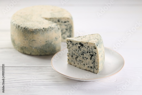Photos A wheel of blue cheese and a slised piece of cheese on a plate on a white wooden