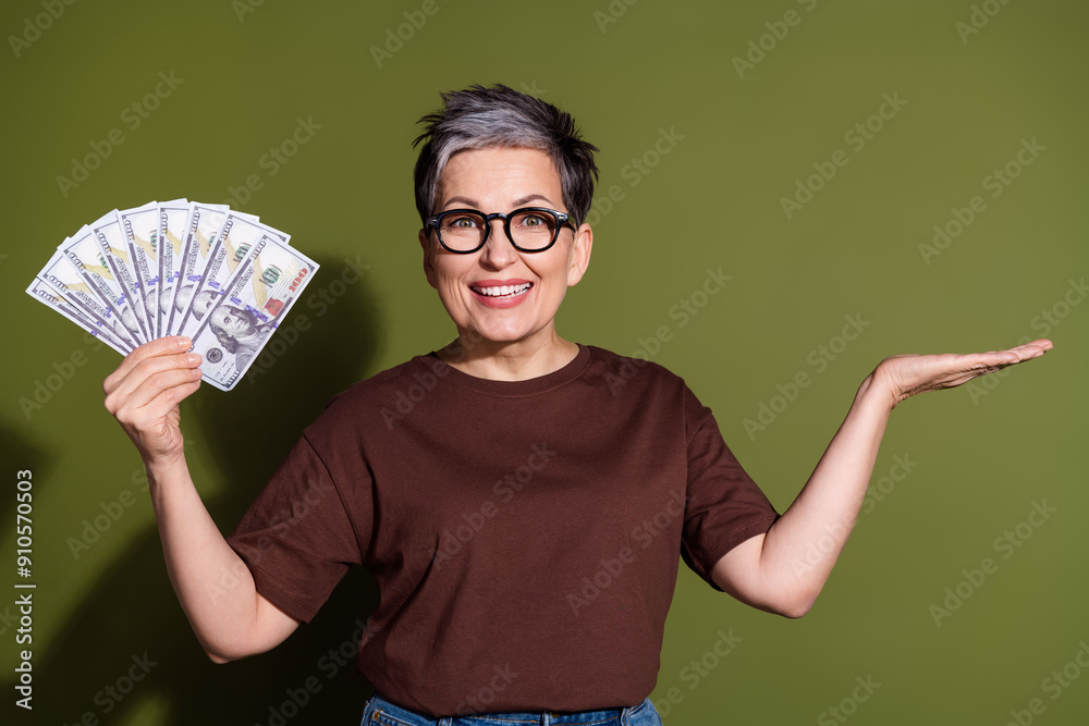 Photo of nice aged woman hold cash empty space wear brown t-shirt isolated on khaki color background Photo of nice aged woman hold cash empty space wear brown t-shirt isolated on khaki color background