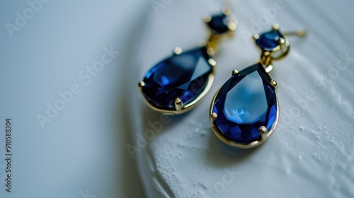 Teardrop-shaped sapphire earrings with a gold setting rest on a white surface