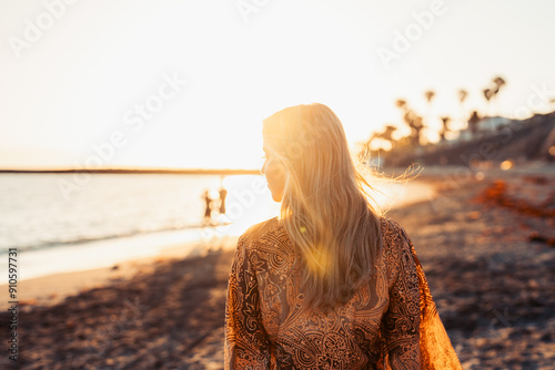 One happy beautiful woman walking on the sand of the beach enjoying and having fun at the sunset of the day. Leisure time on vacations, freedom concept. #910597731