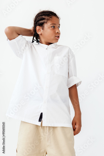 Stylish young boy in white shirt and khaki pants posing against minimalist white wall