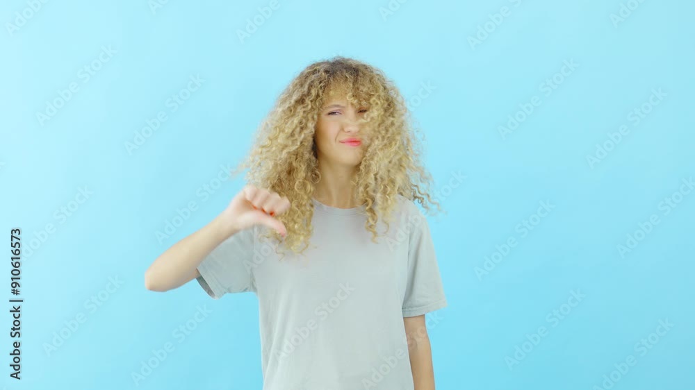 Surprised woman with beautiful curly hair stands confidently against a bright blue background and shows thumbs down Surprised woman with beautiful curly hair stands confidently against a bright blue background and shows thumbs down