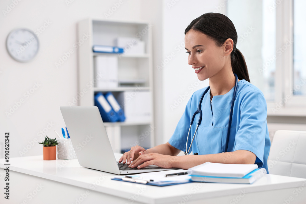 Smiling nurse working with laptop at table in clinic Smiling nurse working with laptop at table in clinic